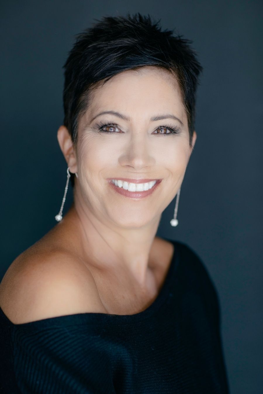 Portrait of a smiling woman with short dark hair and pearl earrings, by Dina Mande